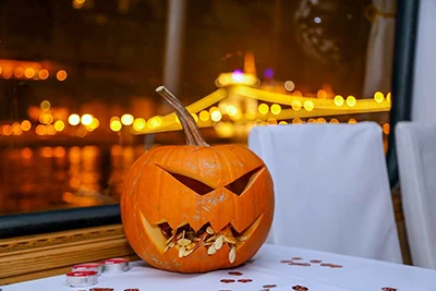 carved pumpkin lantern placed on a white clothed table, the illuminated Chain Bridge can be seen in the background