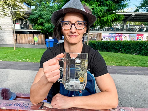 woman wearng glasses and the symbolic grey Oktoberfest hat holding an empty beer mug in her right hand