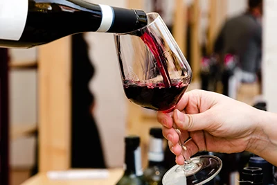 a hand holding a glass into which someone is pouring deep red wine