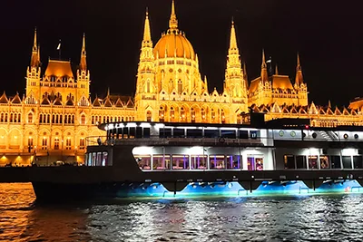 a dinner cruise ship sailing past the lit up Parliament on the Danube
