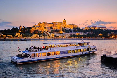 a large white sightseeing boat with open deck sailing on the Danube in Budapest at sunset
