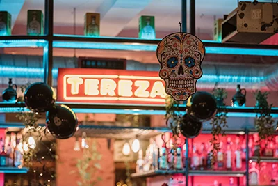 the name of the Mexican restaurant "Tereza" illuminated inside the restaurant above the bar, skull and other Day of the Dead decorations can be seen
