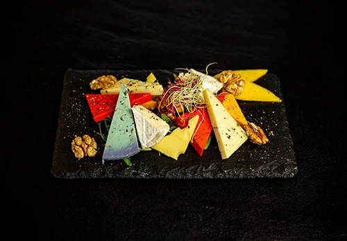 cheese plate consisiting of various triangle shape cheese slice on a black square plate