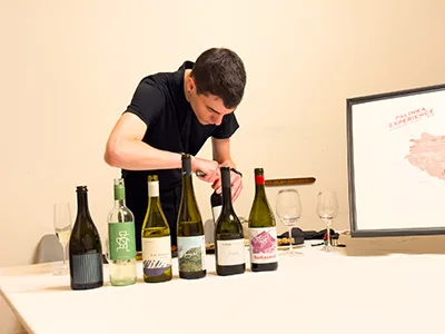 a young male sommelier ttrying to open a bottle of red wine on a wine tasting program (6 bottles of opened wine stand in front of hime