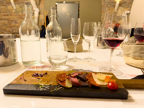 various glasses (white wine, red wine, water, champagne), 2 bottles of mineral water, and the charcuterie plate in the foreground on a wine tasting program