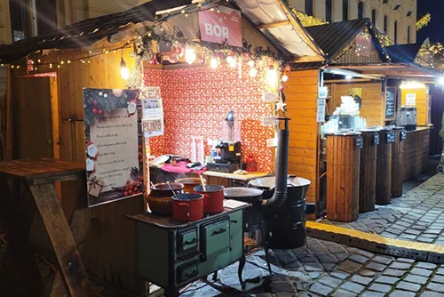 wooden food stall offering mulled wine, lights are on for the night