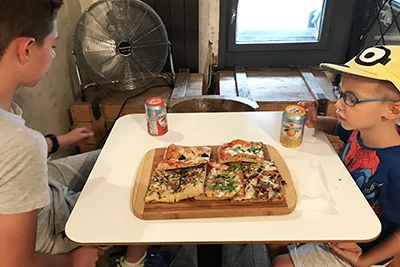 tour two boys sitting at a table in Pizzica: a square pizza slices on a wooden board on the table