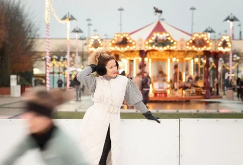 a young woman with balck headphones on skating on the rink on the WestEnd Rooftop Terrace, vintage carousel in the background