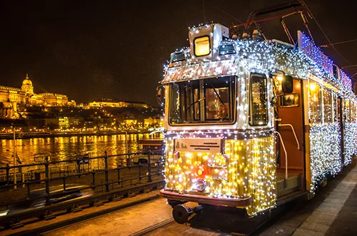 tram 2 decorated with LED lighting travelling on the Pest river bank at night, Buda Castle is visible in the background