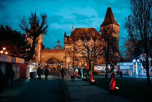 a small Christmas fair in front of Vajdahunyad Castle during the blue hour