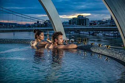 a young couple sipping on champagne in the rooftop jacuzzi of the Rudas Spa