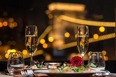 a romantic dinner setting on board a cruise ship: 2 glasses of champagne and a red rose, the illuminated Chain Bridge can be seen in the background