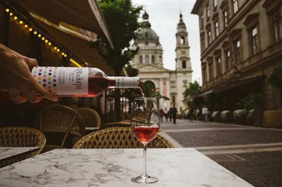 someone - possibly a waiter- pooring rose wine into a glass placed on a marble topped table on the terrace of a restaurant, the Basilica is visible in the background