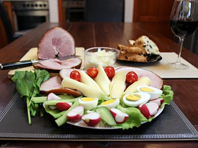 a ham and cheese plate with boiled egg cucumber slices, tomato and lettuce, a glass of red wine placed to the right