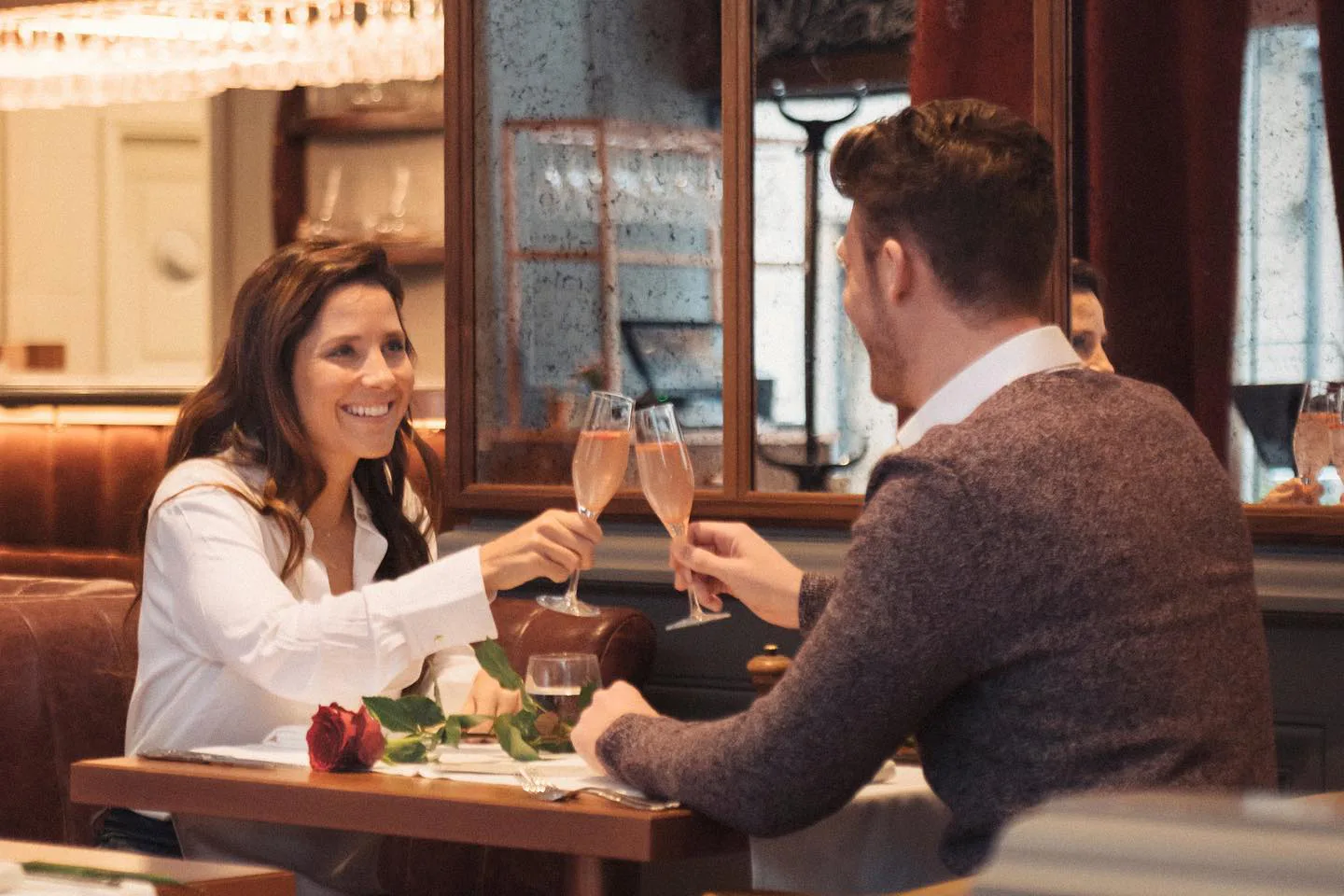 a young couple toasting with a glass of champagne in Ottimo Itailan restaurant, a red rose is lying on the table between them