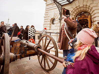 two kids looking at a cannon on display with a hussar in period costume standing next to it