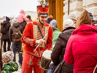 a recruiting hussar in red costume and shako with a small drum hanging from his neck