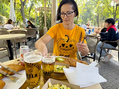 a middle-aged woman with glasses and wearing a yellow t-dhirt eating huge breaded pork chops at Buja Disznok in City park
