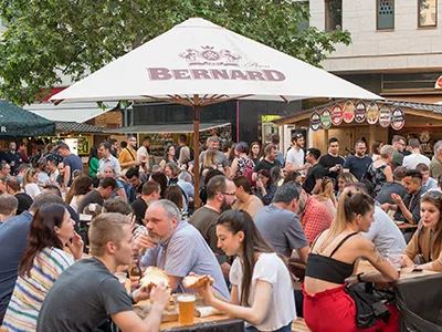 Lots of people eating aand drinking beer at tables on the outdoor Corvin Beer Festival, the beige shade of the Bernard beer maker is in the centre of the photo