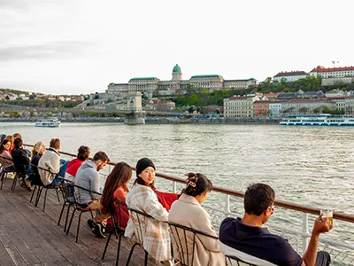 guests sitting in chairs and admiring the view on the open deck of the Széchenyi excursion boat, the Royal Palace can be seen in the Buda side