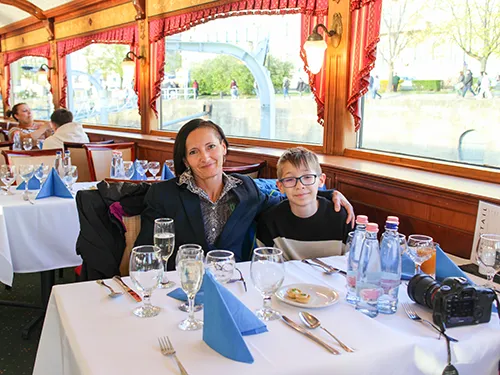 a mother (with medium length dark hair) and her teenage son (blond with glasses) sitting at a dinner table on a cruise ship