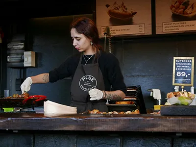 a young female chef wearing black clothes and apron preparing food in a restaurant