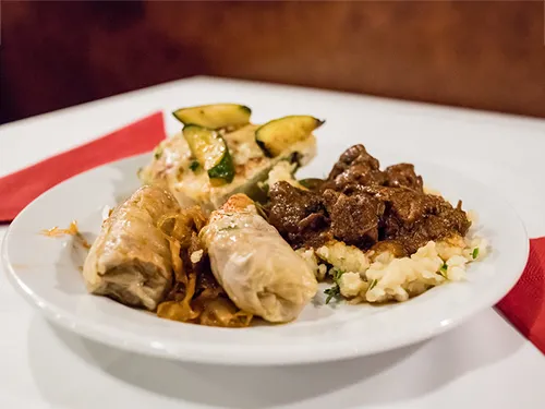 two portions of stuffed cabbage, beef paprikash with noodles on a plate