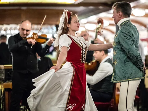 a young woman and a man performing folk dance in Hungarian folk costume, an gypsy band is playing in the background