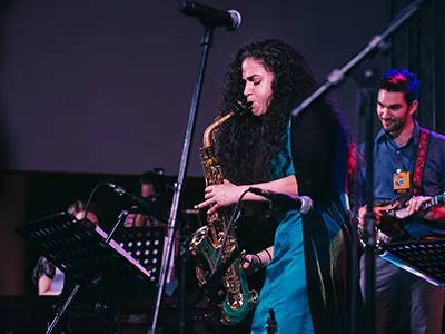 A dark, curly haired woman playing on saxophone, possibly on a concert