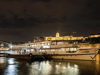 The Count Szechenyi cruise boat on the Danube neear the Chain Bridge at night, The illuminated Royal Palace in Buda is visible in the background